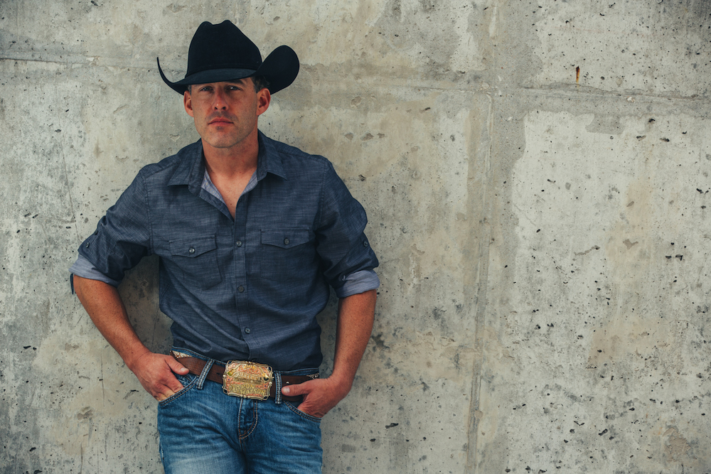 Country music singer Aaron Watson stands against a wall.